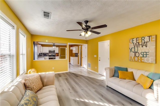 living room featuring light wood-type flooring, ceiling fan, and a textured ceiling