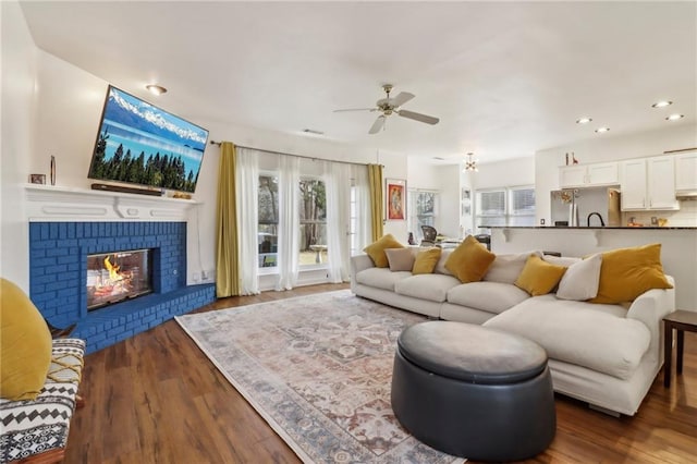 living room with ceiling fan, dark wood-type flooring, and a brick fireplace