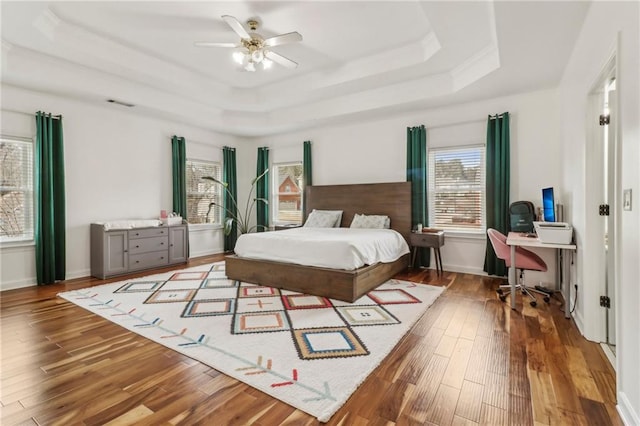 bedroom with ceiling fan, a raised ceiling, and wood-type flooring