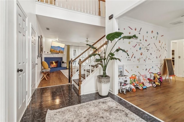 foyer with crown molding, ceiling fan, a brick fireplace, and dark hardwood / wood-style flooring