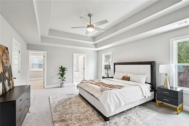 bedroom featuring baseboards, a tray ceiling, ceiling fan, light carpet, and connected bathroom