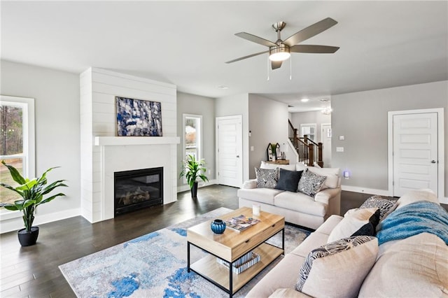 living room featuring baseboards, stairs, wood finished floors, a glass covered fireplace, and a ceiling fan