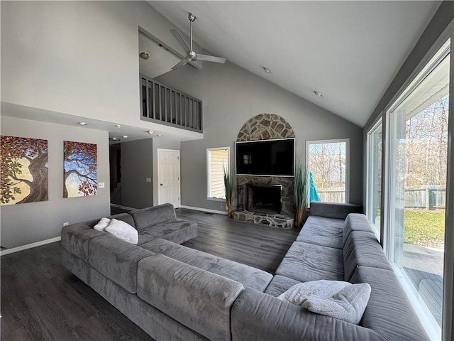 living area featuring lofted ceiling, baseboards, wood finished floors, and a stone fireplace