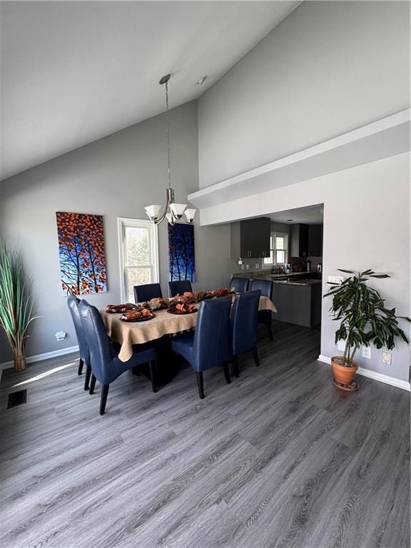 dining area with high vaulted ceiling, a notable chandelier, wood finished floors, visible vents, and baseboards