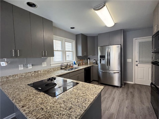 kitchen featuring black appliances, a peninsula, a sink, and light stone countertops