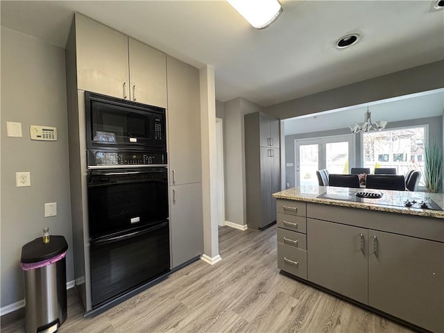 kitchen featuring light stone counters, a notable chandelier, gray cabinetry, light wood-style floors, and black appliances