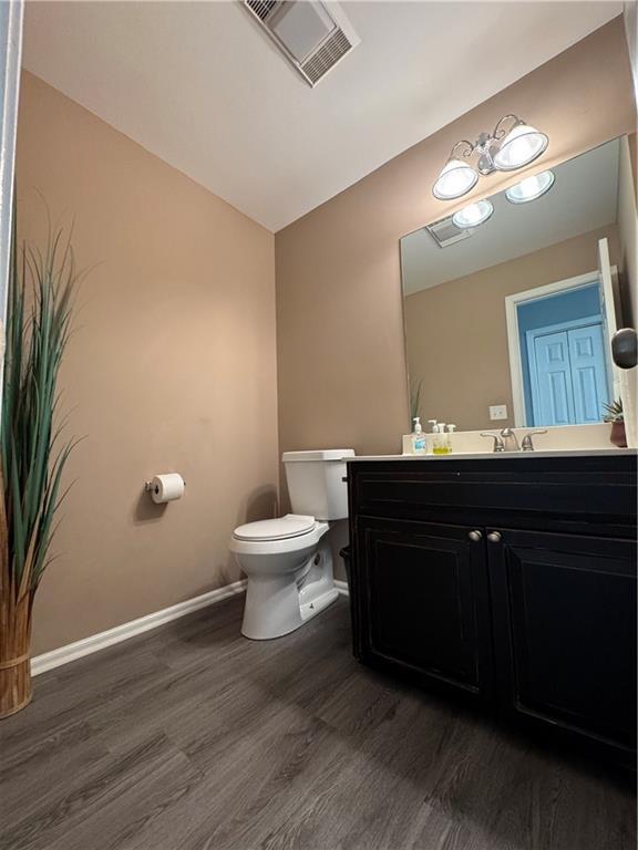 half bathroom featuring baseboards, visible vents, toilet, wood finished floors, and vaulted ceiling