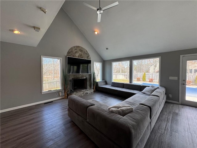 living room with a fireplace with raised hearth, high vaulted ceiling, wood finished floors, visible vents, and baseboards