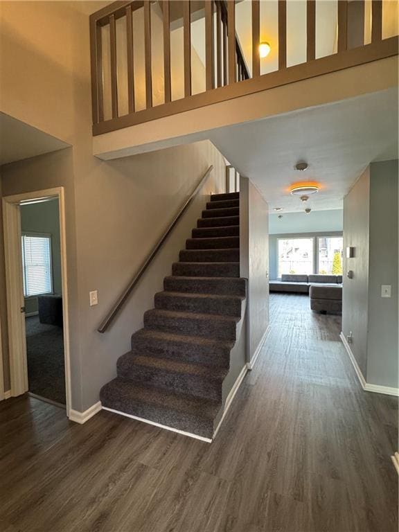 staircase featuring a towering ceiling, baseboards, and wood finished floors