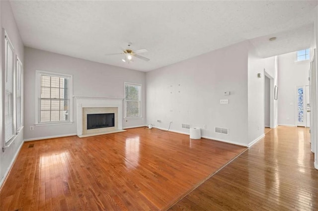 unfurnished living room with ceiling fan, visible vents, a fireplace, and hardwood / wood-style flooring