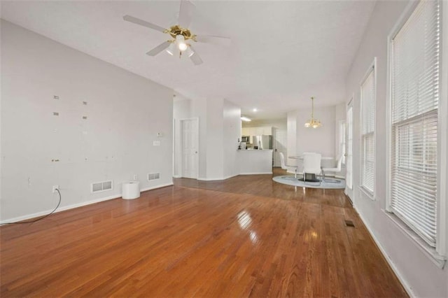 unfurnished living room with ceiling fan with notable chandelier, wood finished floors, visible vents, and baseboards