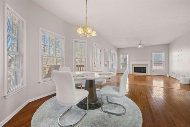 dining area with hardwood / wood-style flooring, a fireplace, baseboards, and ceiling fan with notable chandelier