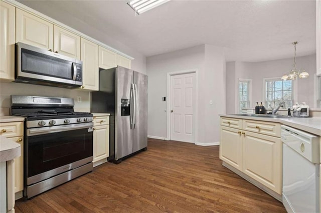 kitchen with dark wood-type flooring, stainless steel appliances, cream cabinetry, light countertops, and a sink