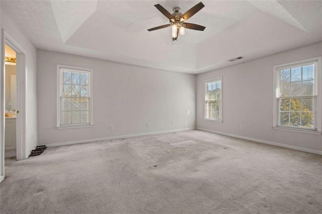 carpeted spare room with a raised ceiling, visible vents, ceiling fan, and baseboards