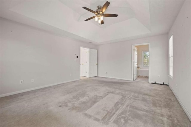 carpeted empty room featuring a ceiling fan, a tray ceiling, and baseboards