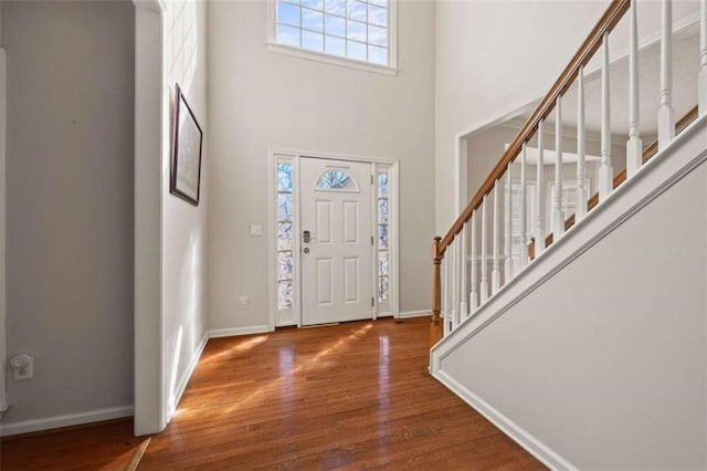 entrance foyer featuring a towering ceiling, stairway, baseboards, and wood finished floors