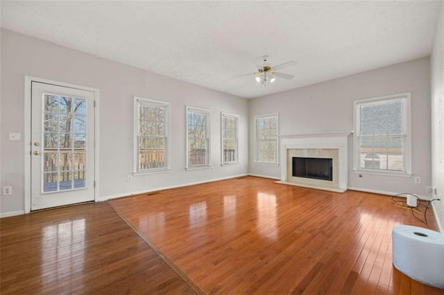 unfurnished living room featuring a high end fireplace, plenty of natural light, hardwood / wood-style floors, and ceiling fan