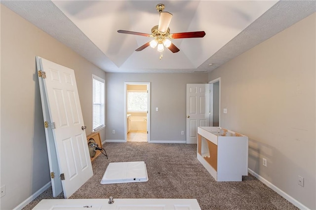 bedroom with carpet flooring, a tray ceiling, ensuite bath, and ceiling fan