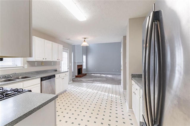 kitchen with sink, a textured ceiling, a fireplace, white cabinets, and appliances with stainless steel finishes