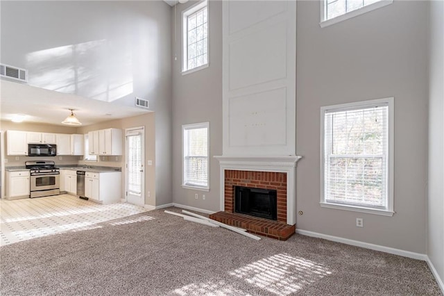 unfurnished living room with light carpet, a high ceiling, a brick fireplace, and plenty of natural light