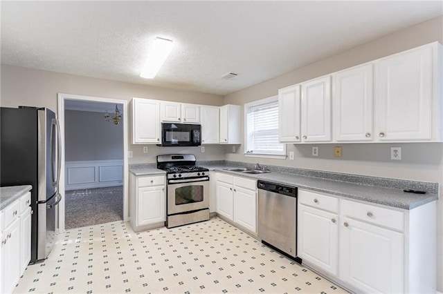 kitchen featuring appliances with stainless steel finishes, a textured ceiling, white cabinetry, and sink