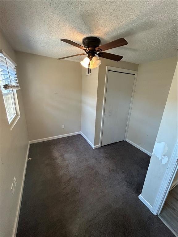 1182 Sims St SW, Atlanta, GA 30310 - unfurnished bedroom featuring baseboards, a textured ceiling, dark carpet, a ceiling fan, and a closet