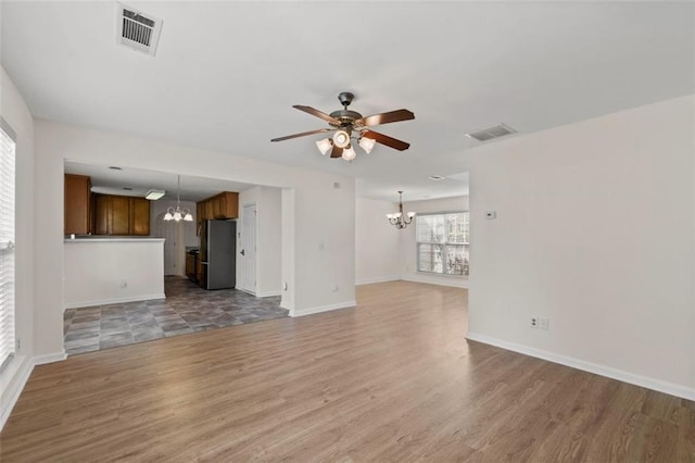 unfurnished living room with light wood finished floors, visible vents, and ceiling fan with notable chandelier