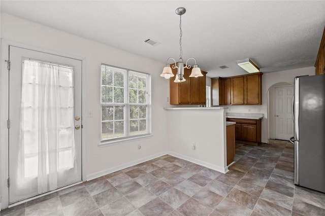 kitchen featuring pendant lighting, a notable chandelier, visible vents, brown cabinetry, and freestanding refrigerator