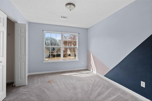 spare room with a textured ceiling, carpet, visible vents, and baseboards