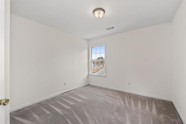 spare room with carpet floors, baseboards, visible vents, and a textured ceiling