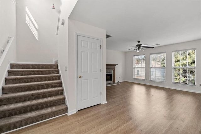 stairs featuring wood finished floors, plenty of natural light, a fireplace with flush hearth, and a ceiling fan