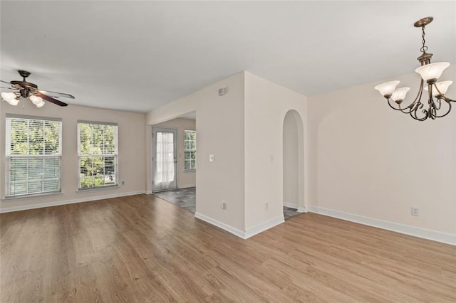 unfurnished living room with arched walkways, baseboards, light wood finished floors, and ceiling fan with notable chandelier