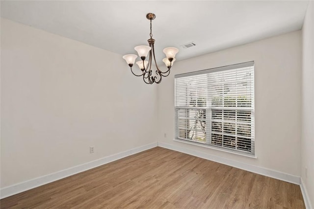 spare room with a chandelier, visible vents, baseboards, and wood finished floors