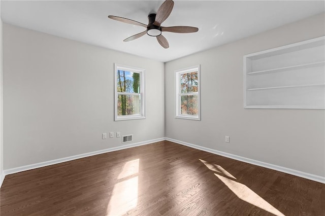 empty room with dark wood-style floors, visible vents, ceiling fan, and baseboards