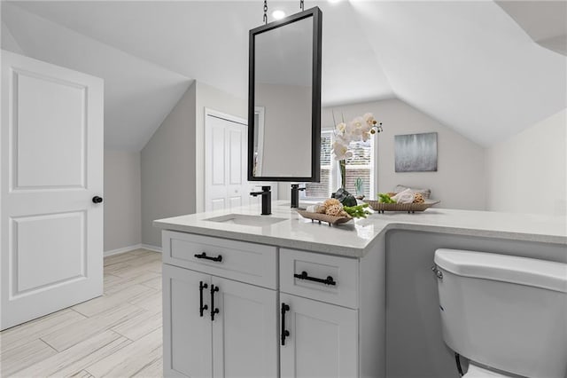 bathroom with baseboards, toilet, vanity, and lofted ceiling