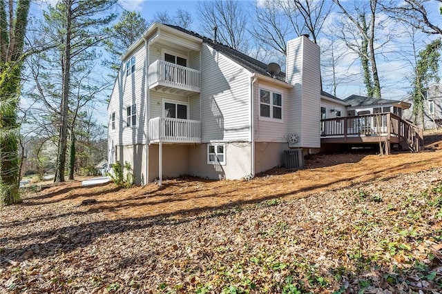 back of house featuring central AC unit, a chimney, and a balcony