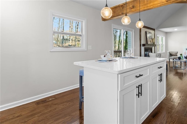 kitchen featuring visible vents, dark wood-type flooring, baseboards, lofted ceiling with beams, and a glass covered fireplace