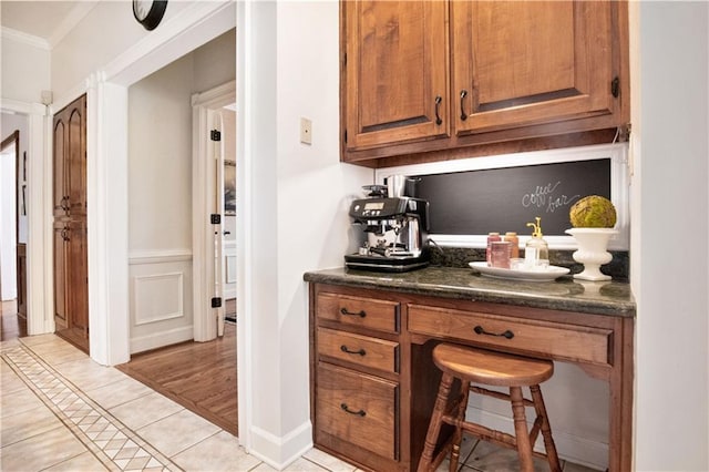 bar featuring light tile patterned flooring, crown molding, and dark stone counters