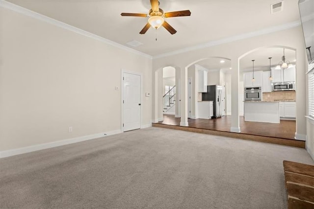 unfurnished living room with ceiling fan, visible vents, arched walkways, stairway, and ornamental molding