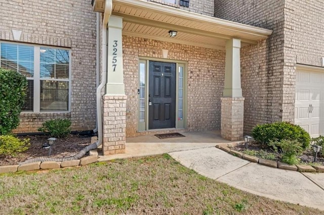view of exterior entry with brick siding, a garage, and a porch