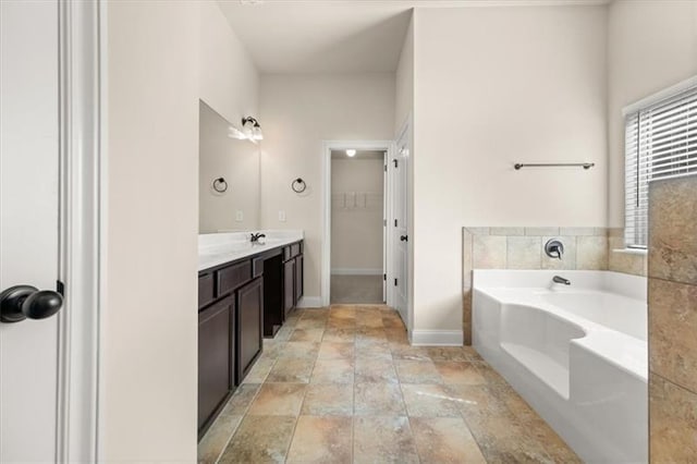 full bathroom with vanity, stone finish floor, baseboards, a spacious closet, and a garden tub
