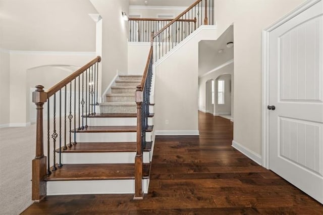 stairs featuring arched walkways, baseboards, wood finished floors, and a towering ceiling