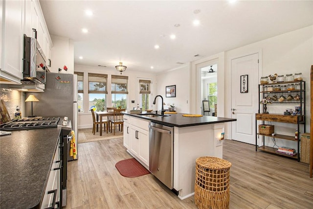 kitchen with dark countertops, a sink, white cabinets, stainless steel appliances, and light wood-style flooring