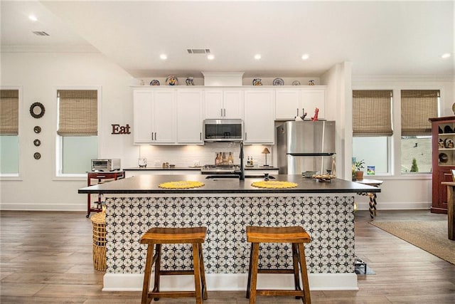 kitchen with a kitchen breakfast bar, visible vents, dark countertops, appliances with stainless steel finishes, and an island with sink