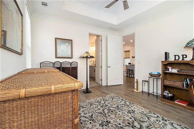 bedroom with visible vents, ornamental molding, wood finished floors, ensuite bathroom, and a raised ceiling