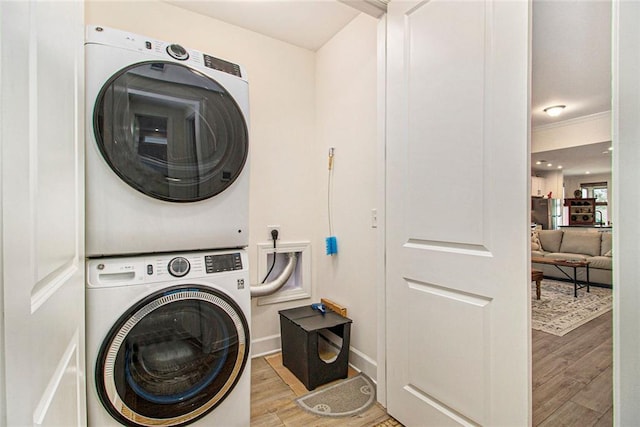 laundry room with laundry area, stacked washer and clothes dryer, light wood-style floors, and baseboards