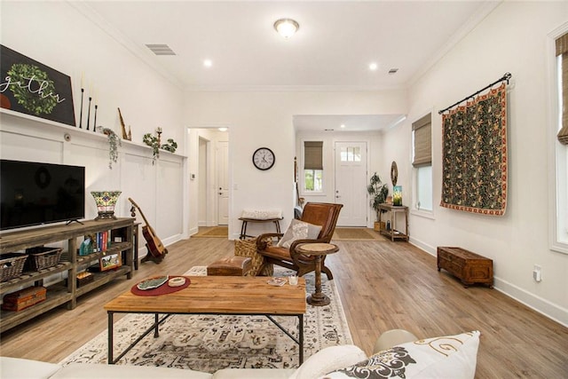 living area with baseboards, visible vents, ornamental molding, and light wood-style floors