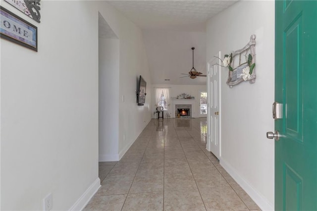 hall with light tile patterned floors, a textured ceiling, lofted ceiling, and baseboards