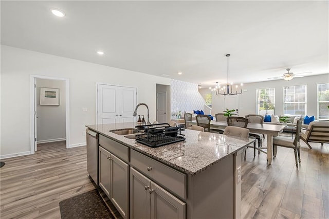 kitchen with a kitchen island with sink, sink, light hardwood / wood-style flooring, and decorative light fixtures