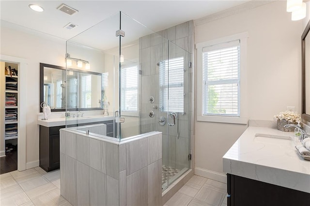 full bathroom featuring visible vents, baseboards, two vanities, a sink, and a stall shower